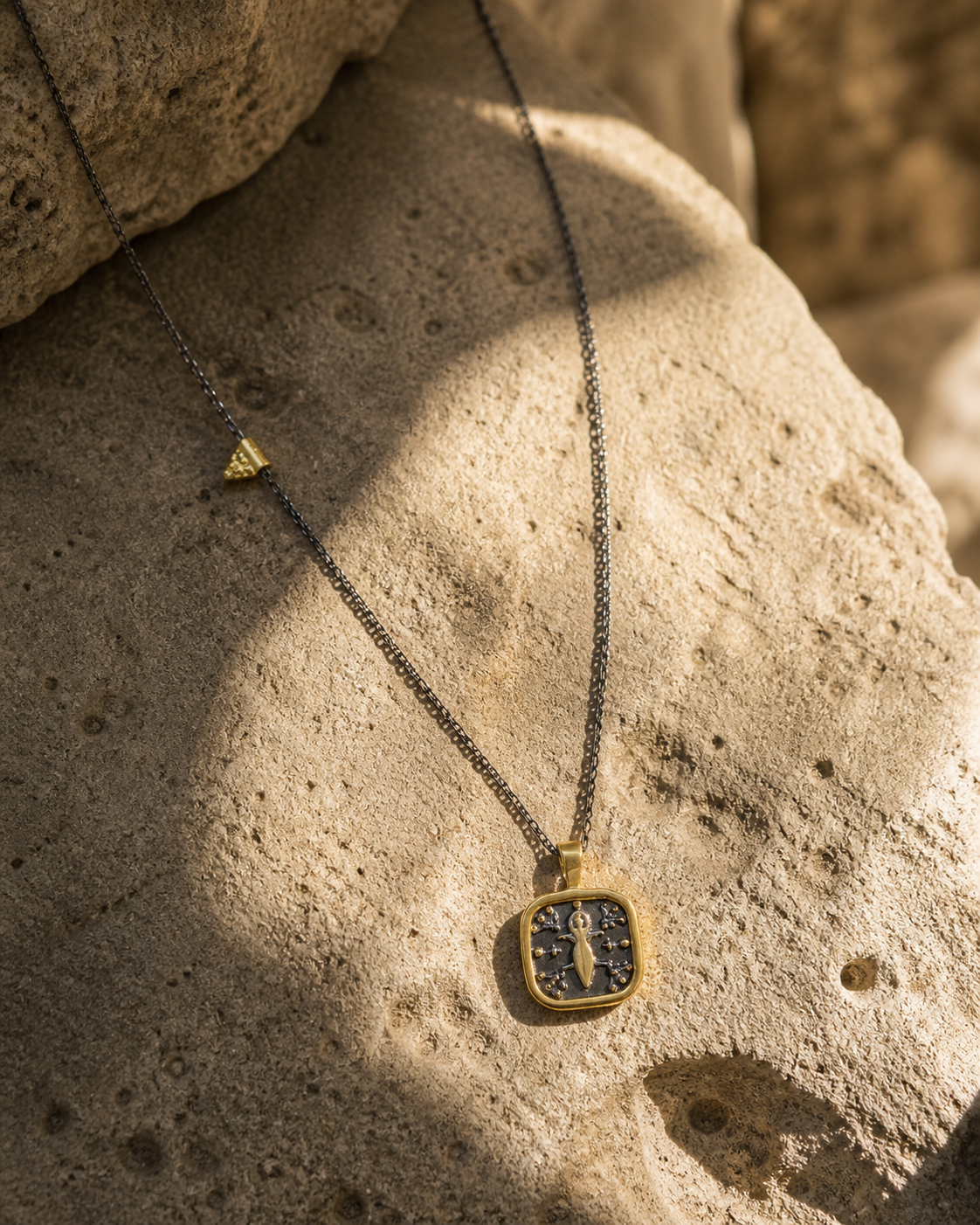 Goddess motif silver necklace with pearl back detail and gold-plated accents on natural stone surface