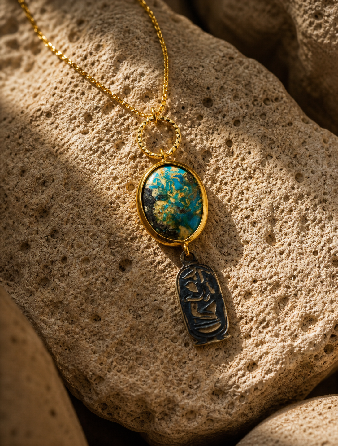 Antique turquoise stone necklace with gold-plated silver details and symbolic charm on natural stone surface