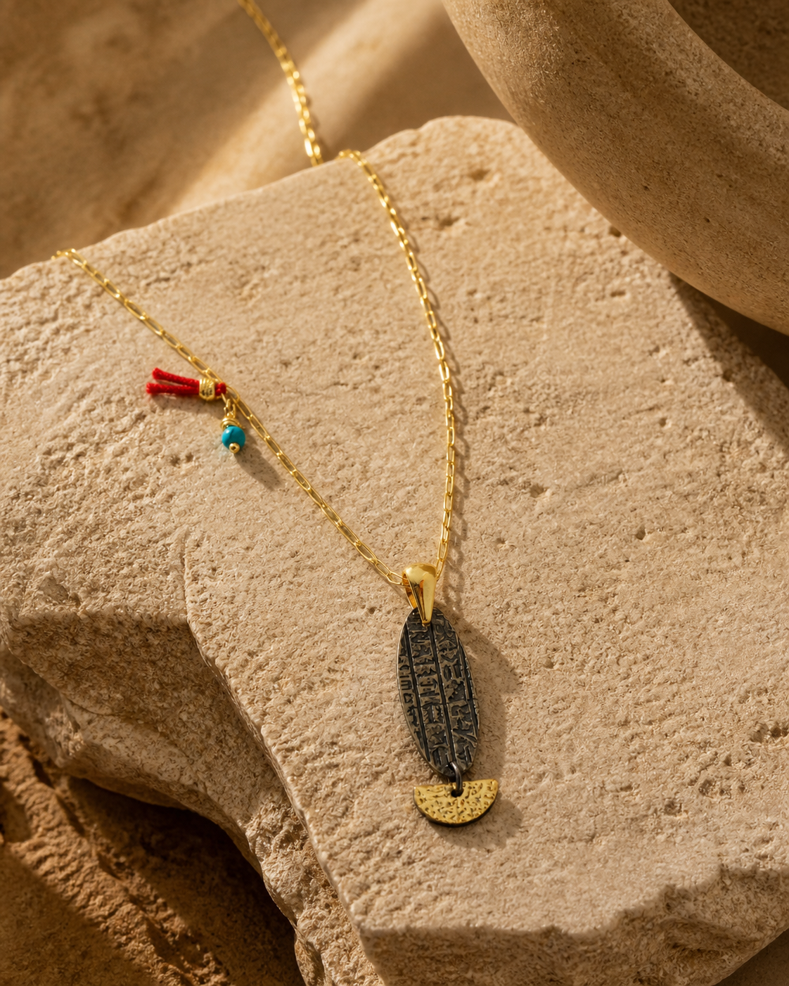 Ancient symbol fish pendant necklace with gold-plated silver chain, oxidized engraved charm and pearl back detail on natural stone surface