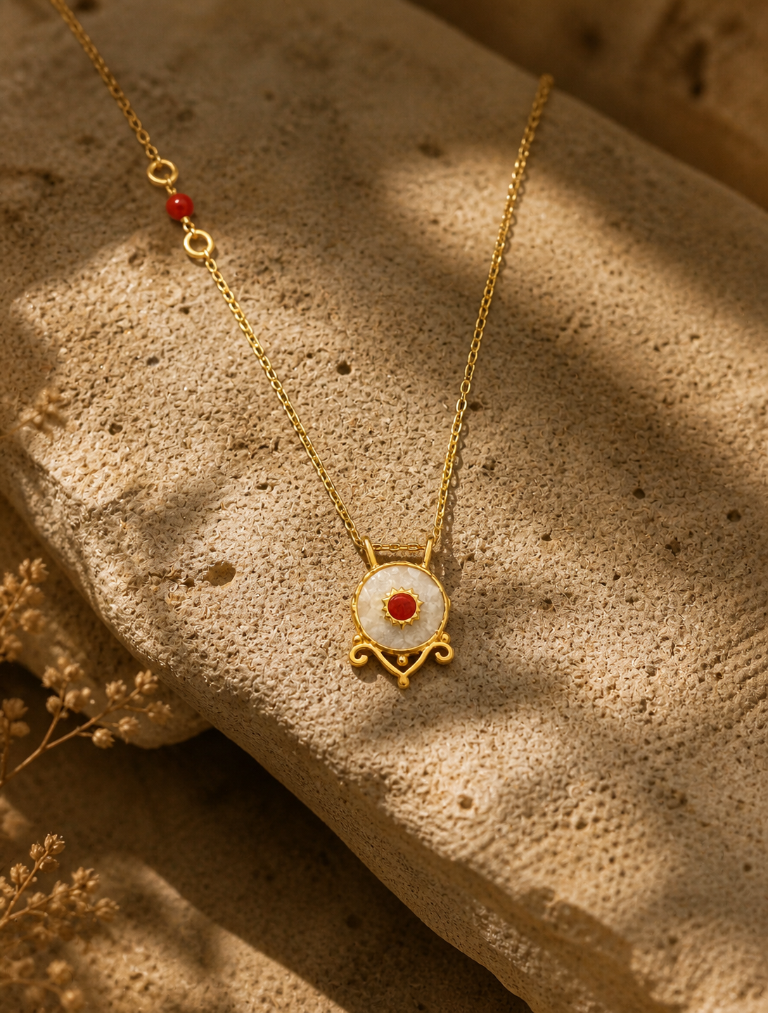 Mother-of-pearl effect necklace with red stone detail and gold-plated silver chain on natural stone surface