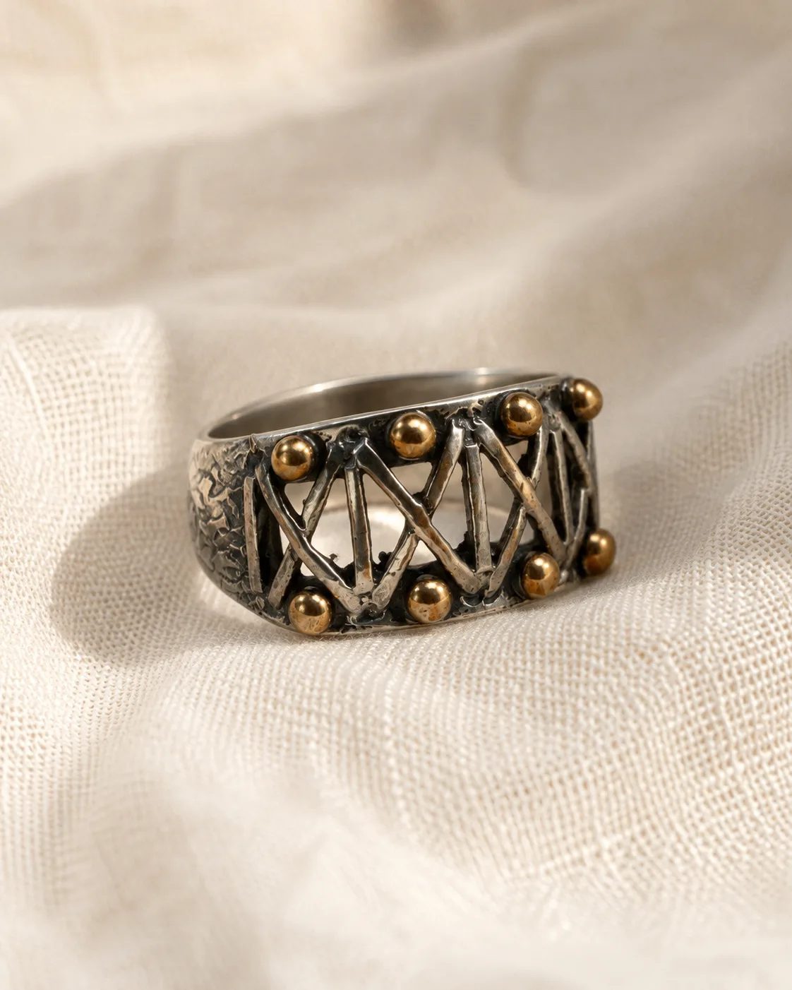 Openwork zigzag silver ring with bronze detail resting on cream linen