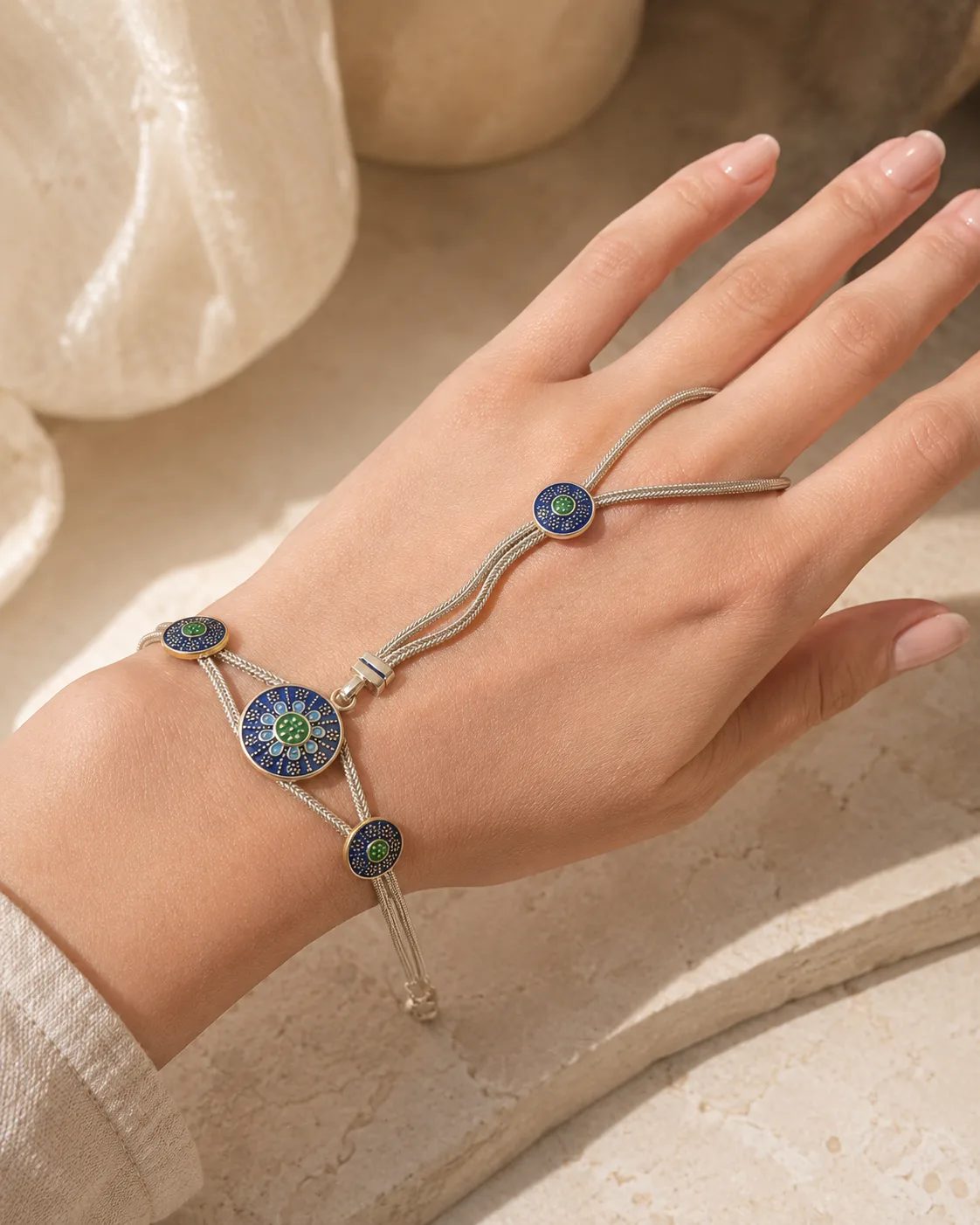 Blue evil eye silver-tone hand chain bracelet worn on a woman’s hand
