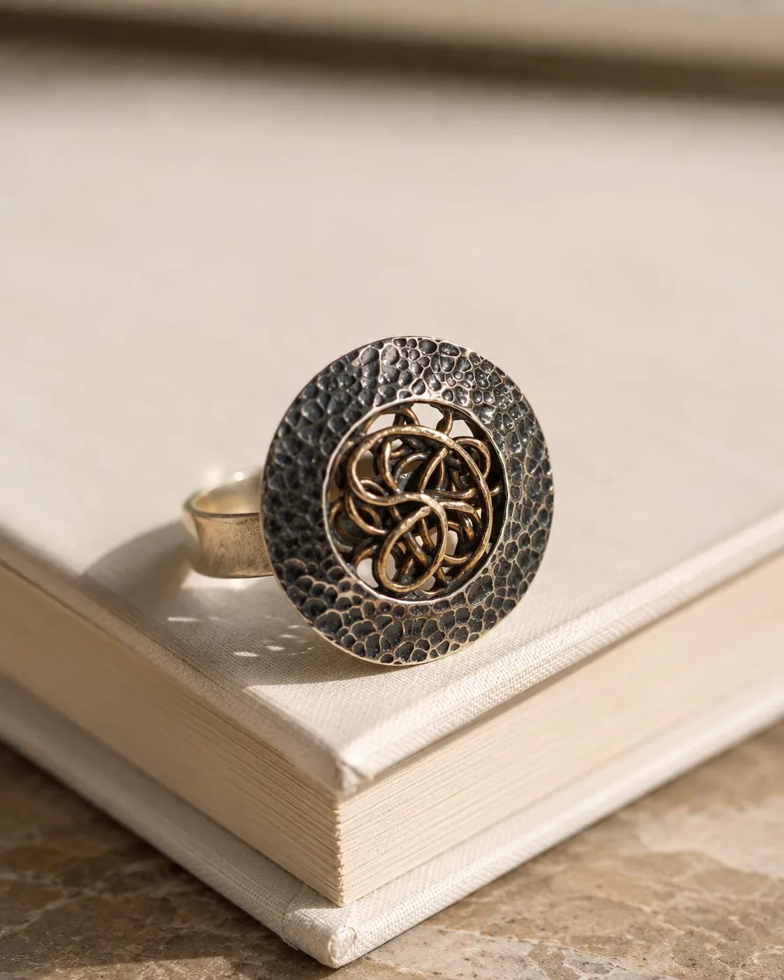 Top view of the hammered silver ring with openwork copper interlace on a stone surface