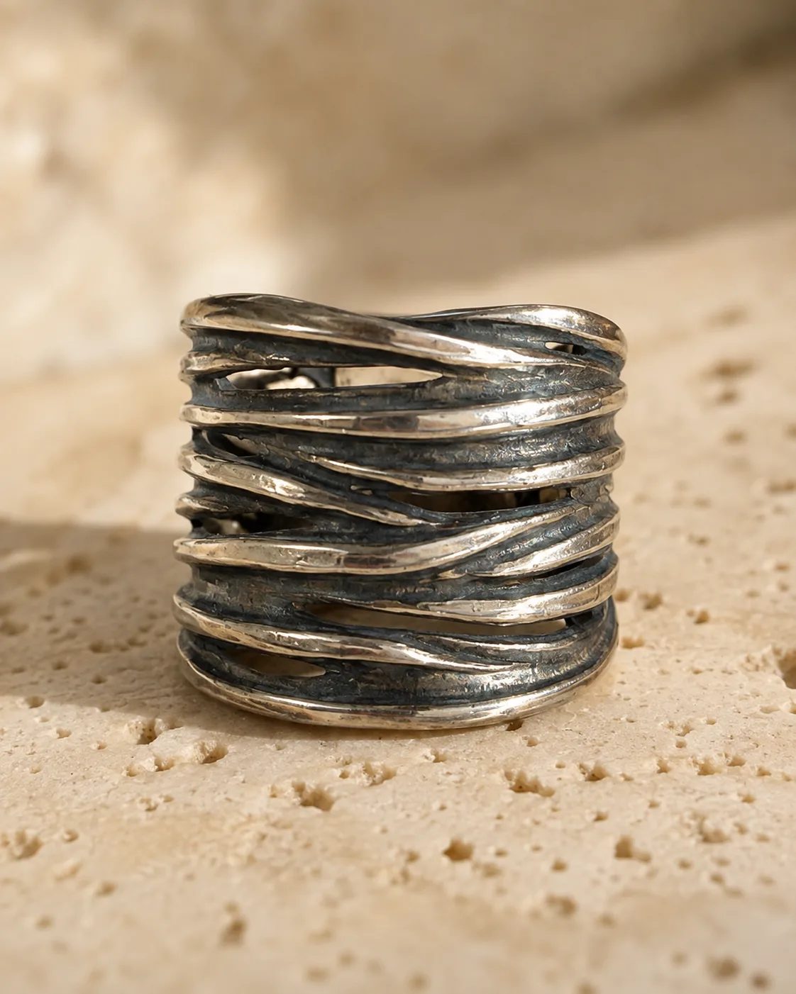Tall sculptural silver ring on a linen-bound book, strands crossing around the band
